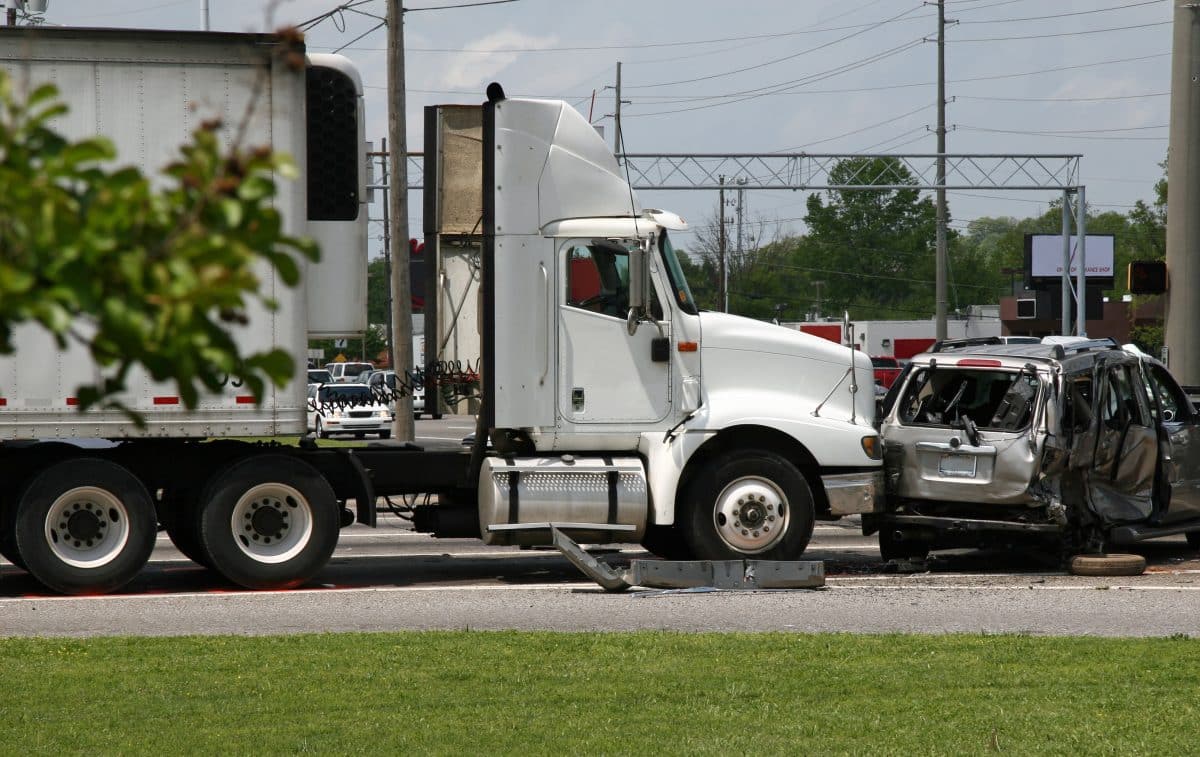 A white semi-truck crashes into a silver SUV causing severe damage to the SUV.