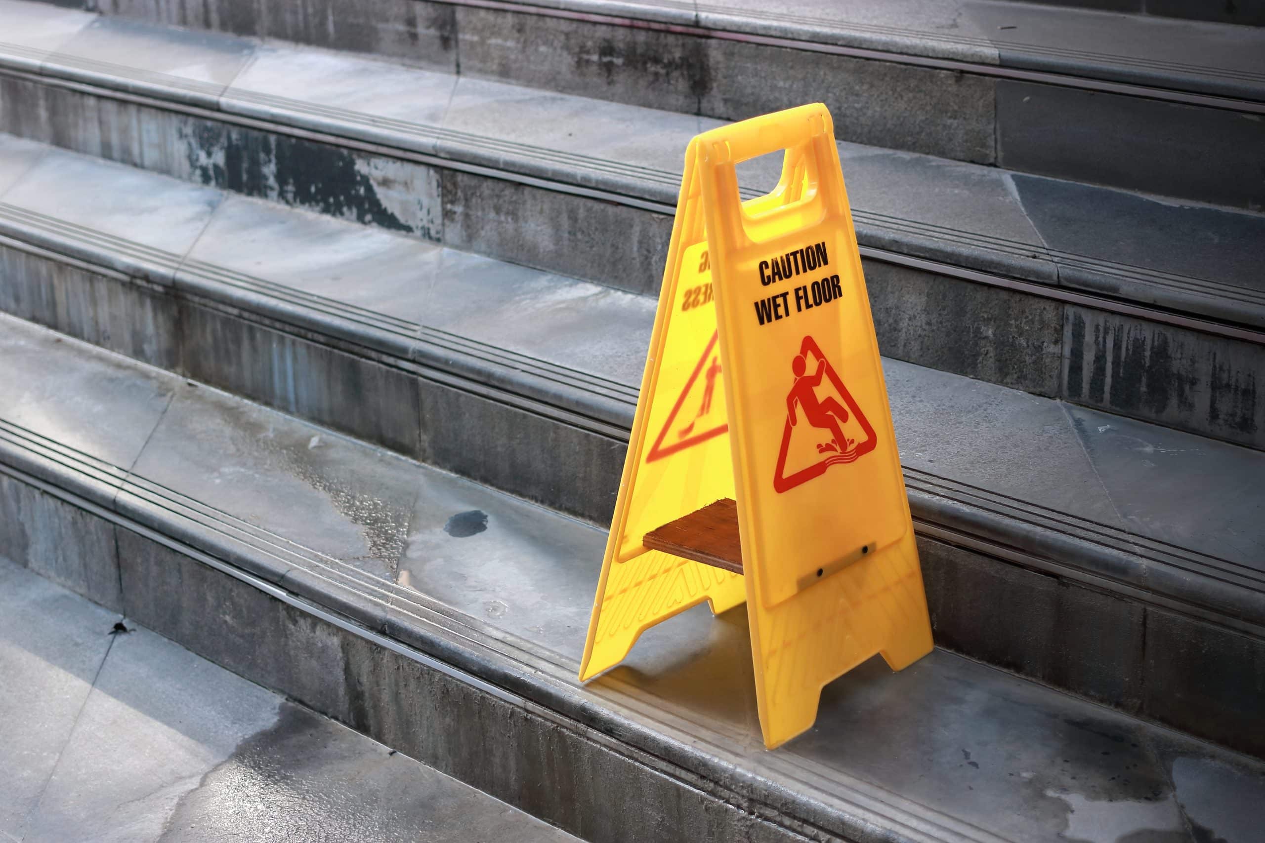 Yellow caution wet floor sign at staircase of outdoor city.