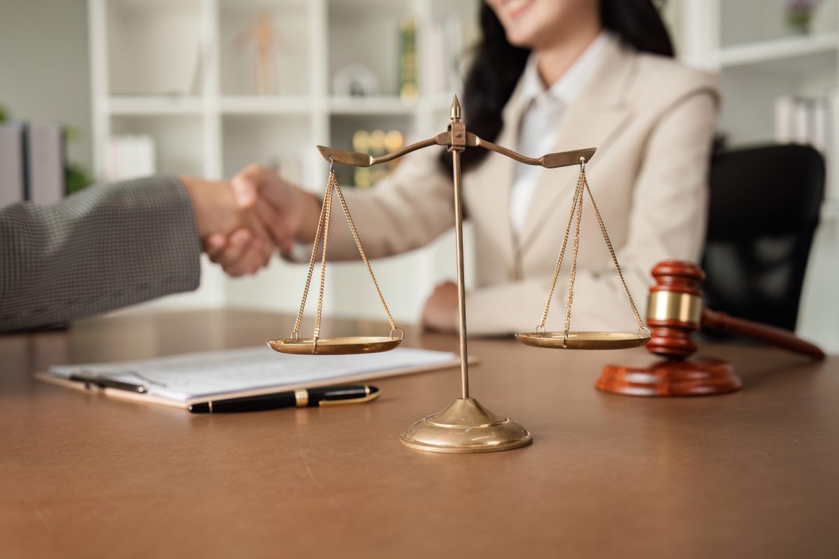 A lawyer sits are her desk and shakes hands with her client.