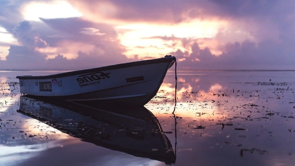 A boat has washed ashore on a beach at sunset.