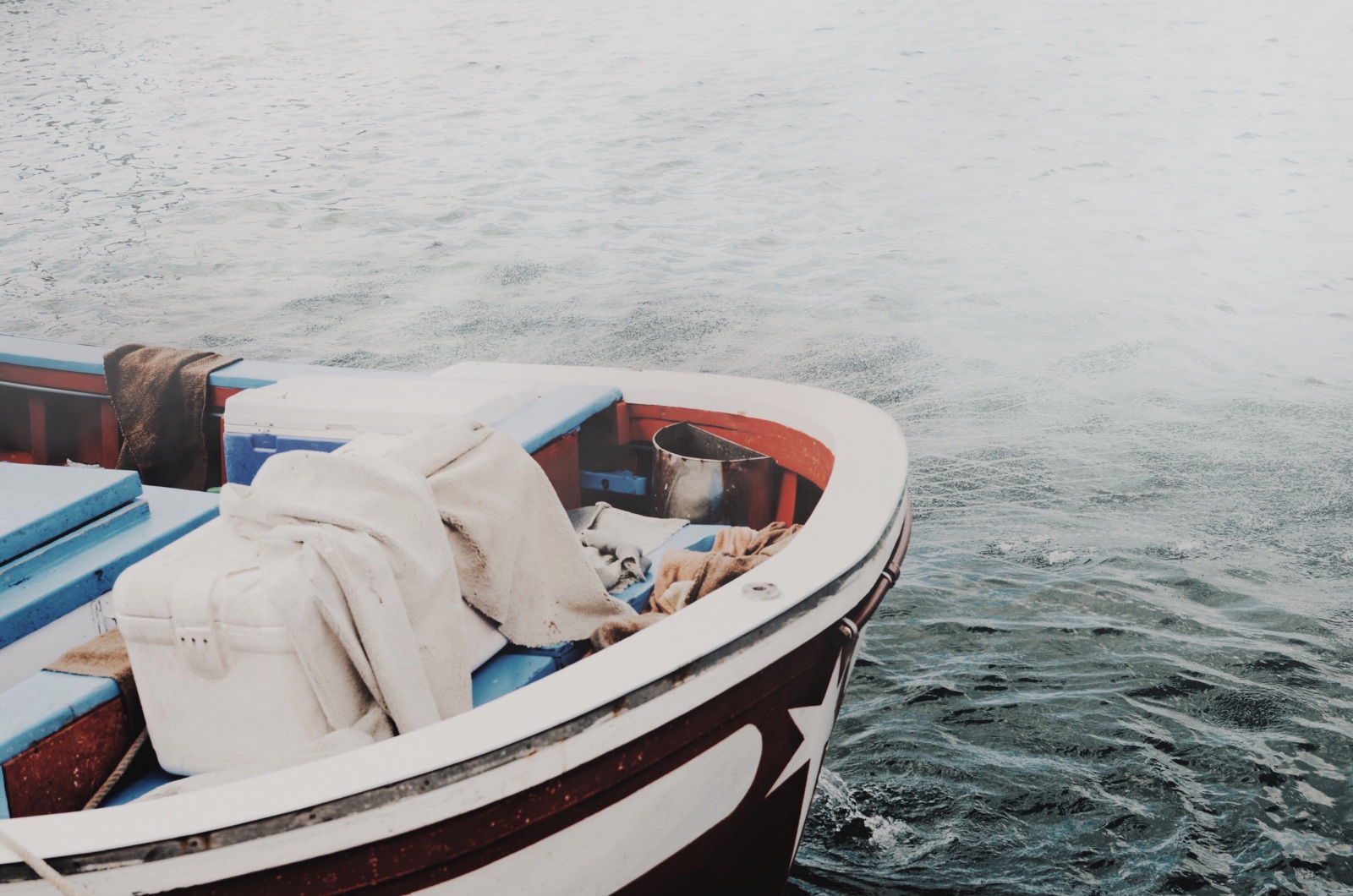 A vacant boat containing a cooler and gear sits on the water.