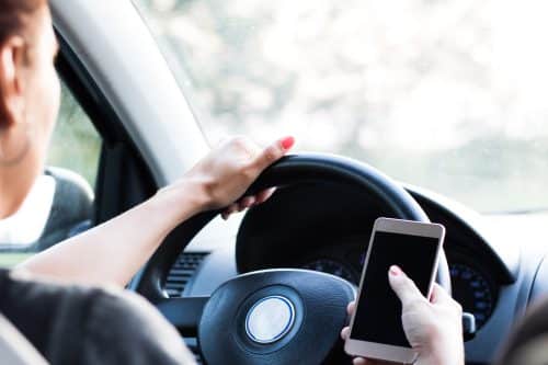 Close up of woman driving car and texting on mobile phone.