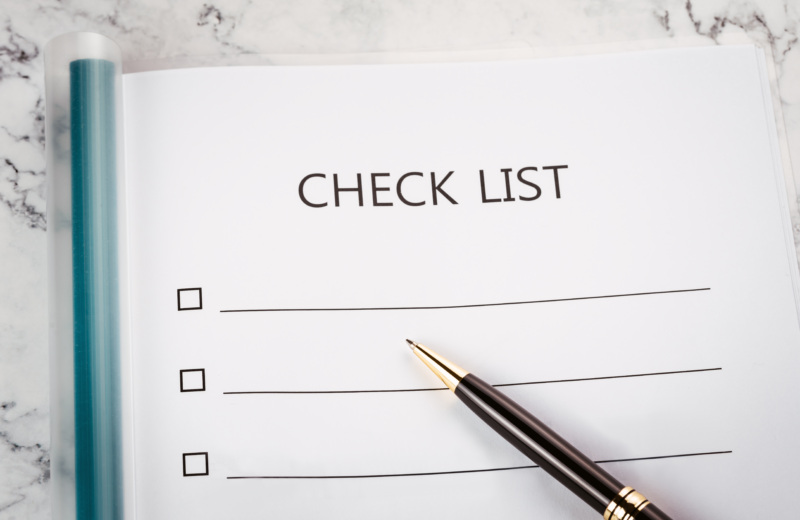 A pen lying on top of a checklist that is sitting on a marble countertop.
