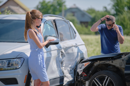 A male and female driver call their insurance companies while standing outside their vehicles looking at the damage from a t-bone accident.