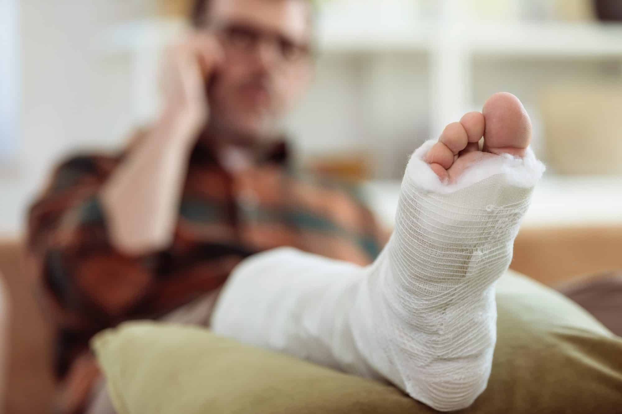 Mature man sits on the couch and talks on the phone while resting his broken foot.