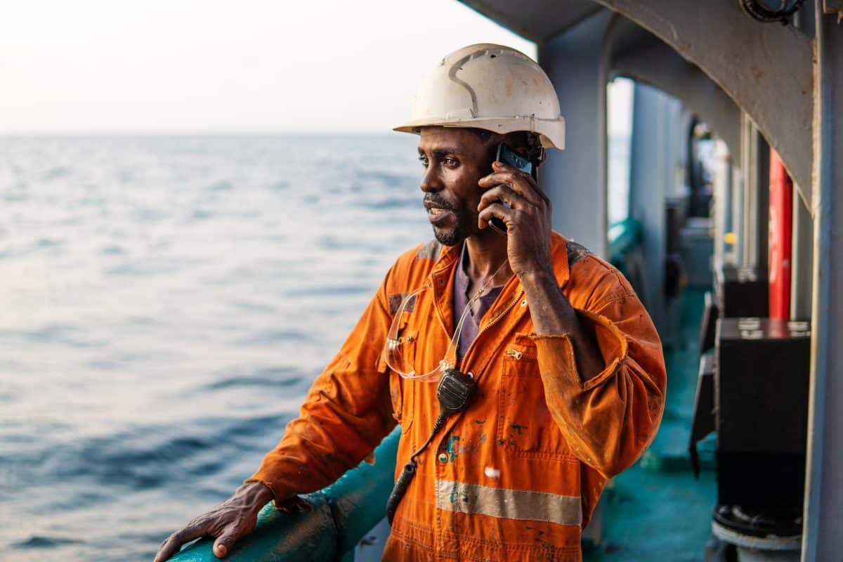 Maritime worker stands on the deck of a vessel calling a maritime injury lawyer on the phone to report a work-related injury.