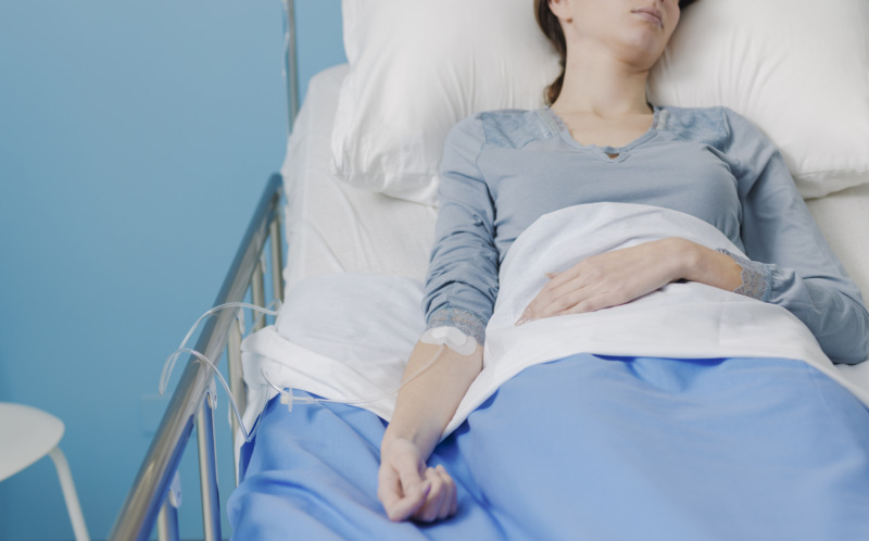 A patient lying in a hospital bed with an IV drip attached to their arm.