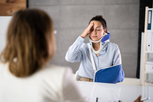 A woman with a neck and arm brace holds her head while speaking with her attorney.