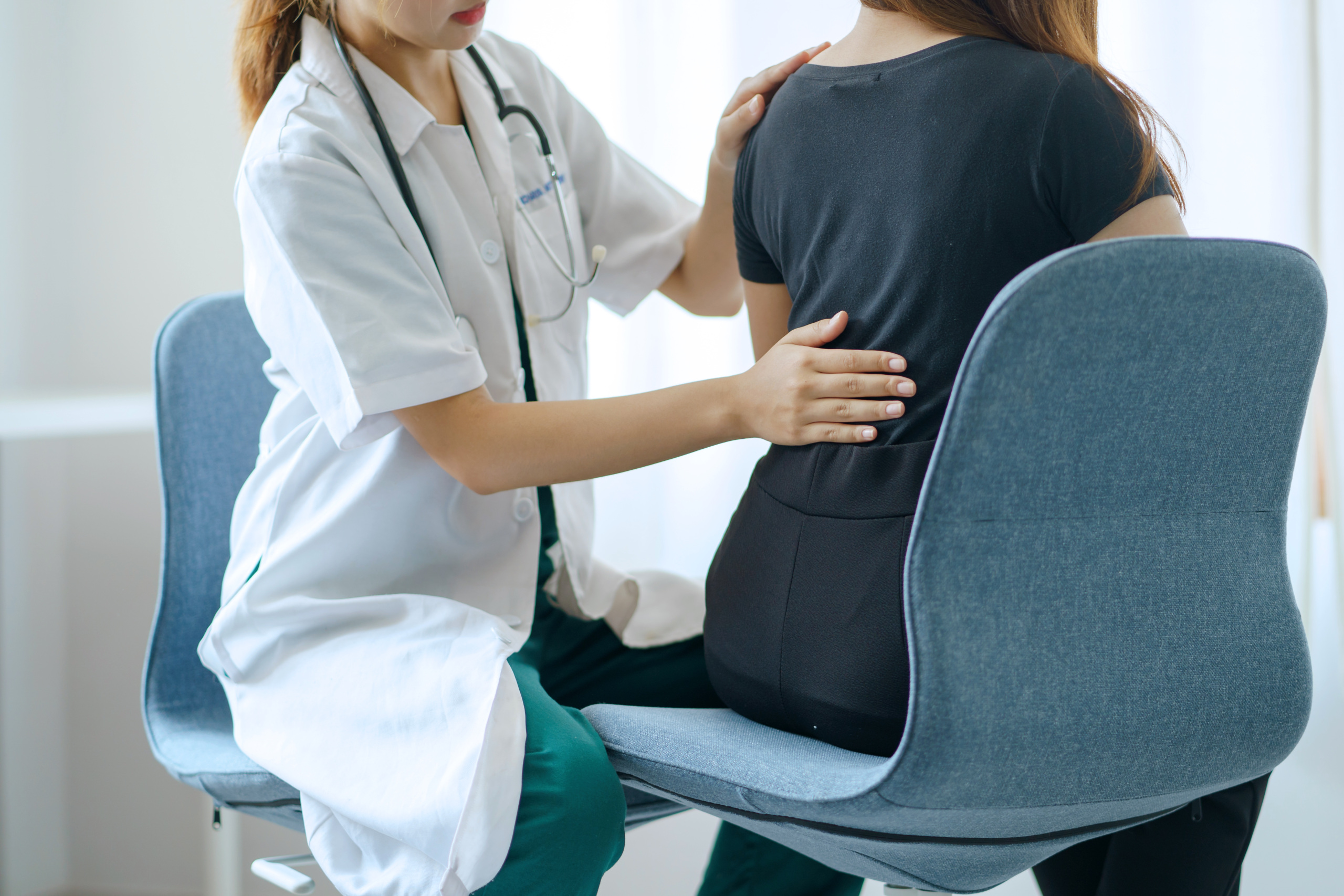 A doctor examining a patient's back while the patient is seated.