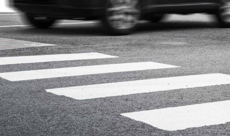 A crosswalk with a car speeding across it.