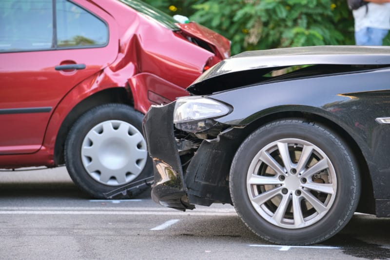 Close-up view of bumper damage to a black sedan and a red sedan after a rear-end collision.