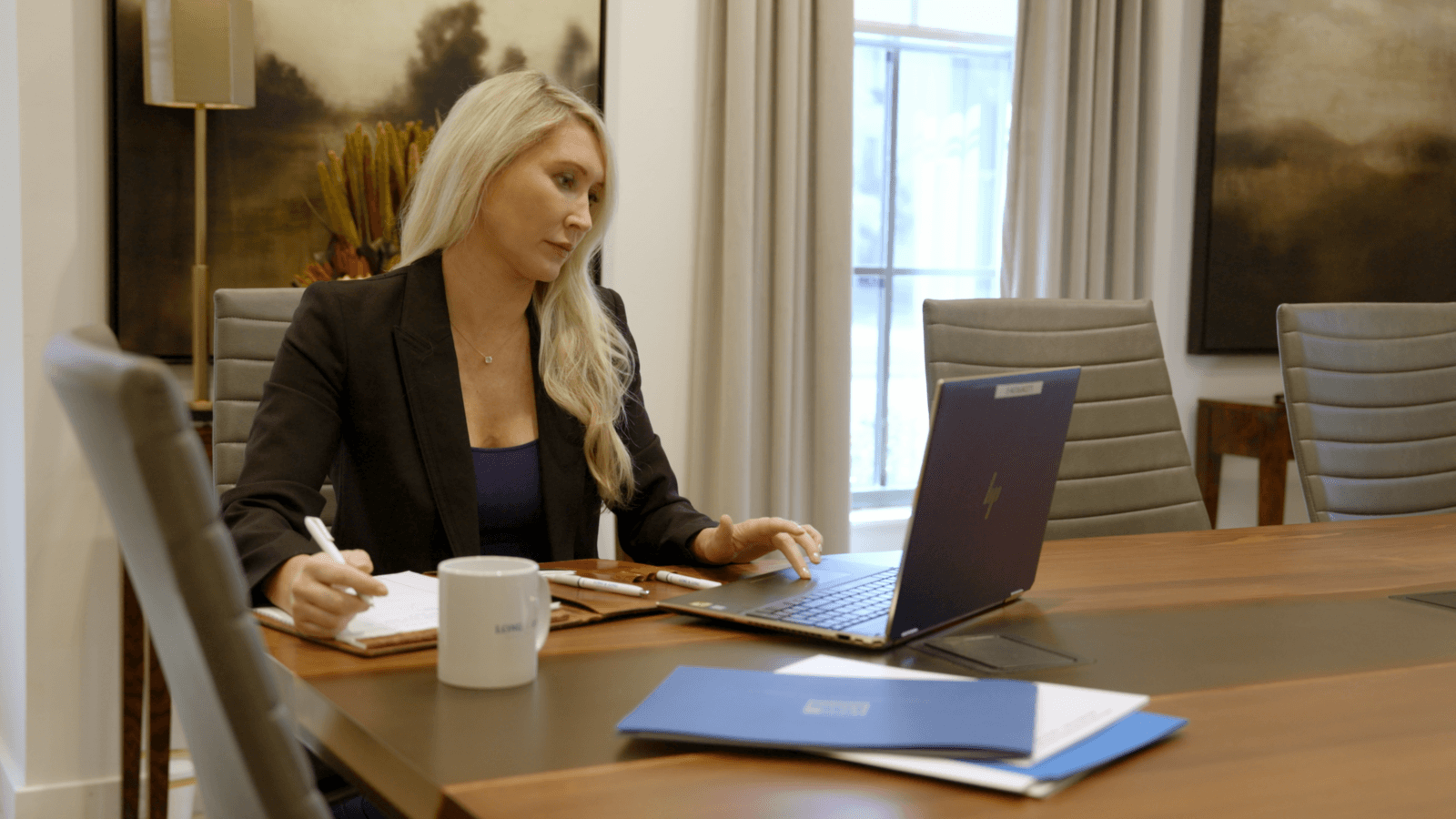 Attorney Cate Biggs of Long & Long Injury Attorneys sits at a conference table reviewing documents on her laptop and taking notes on a legal pad.