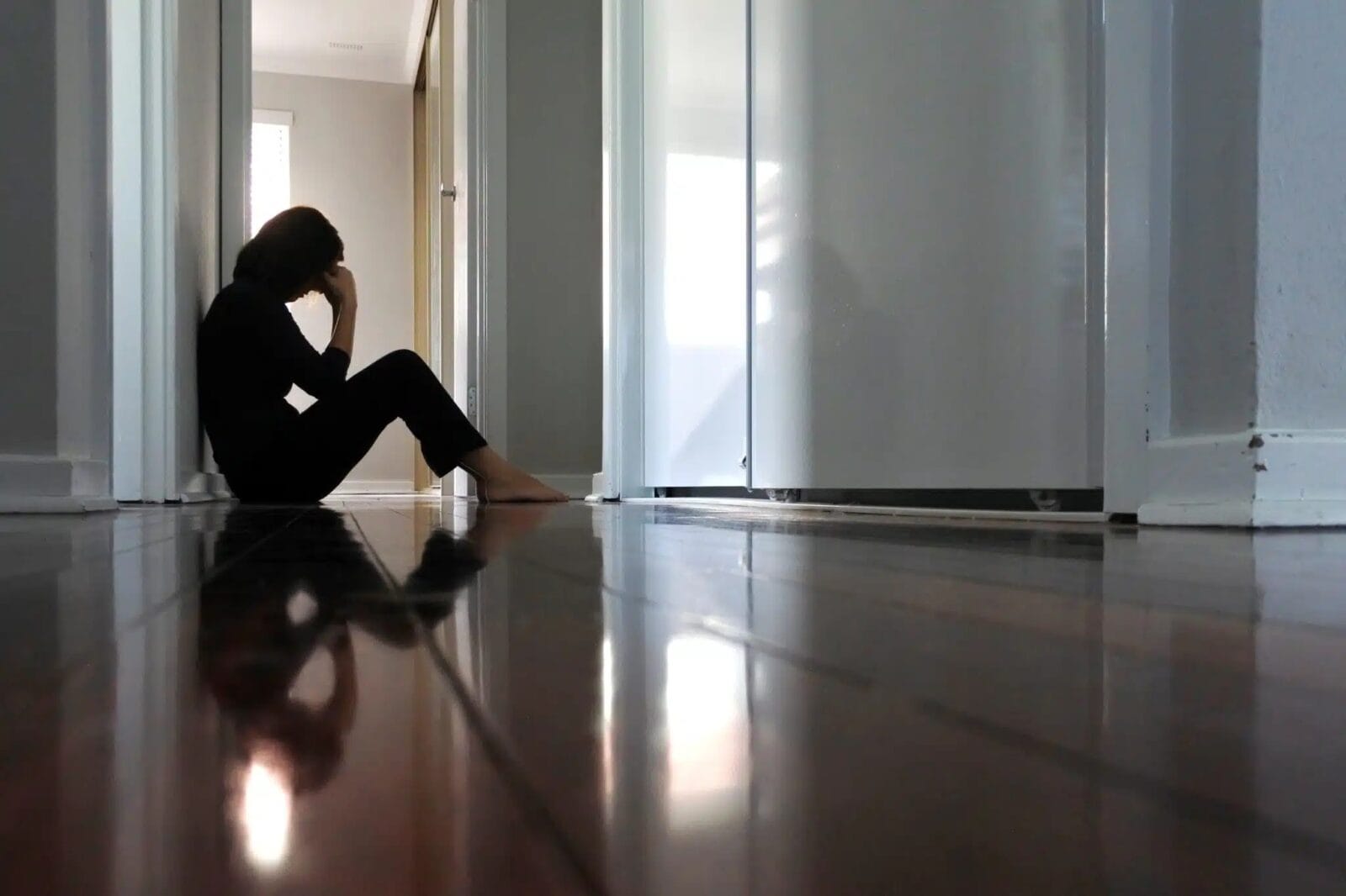 A woman sits on the floor of her home with her head in her hands.