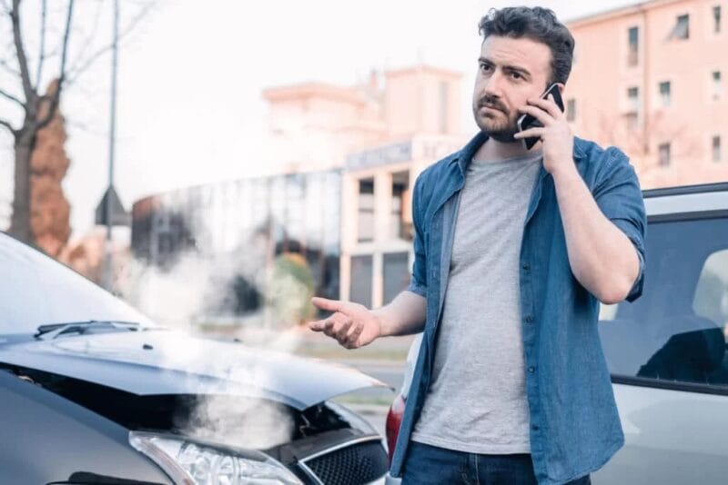 A man stands at the scene of a rear-end collision talking on his phone.