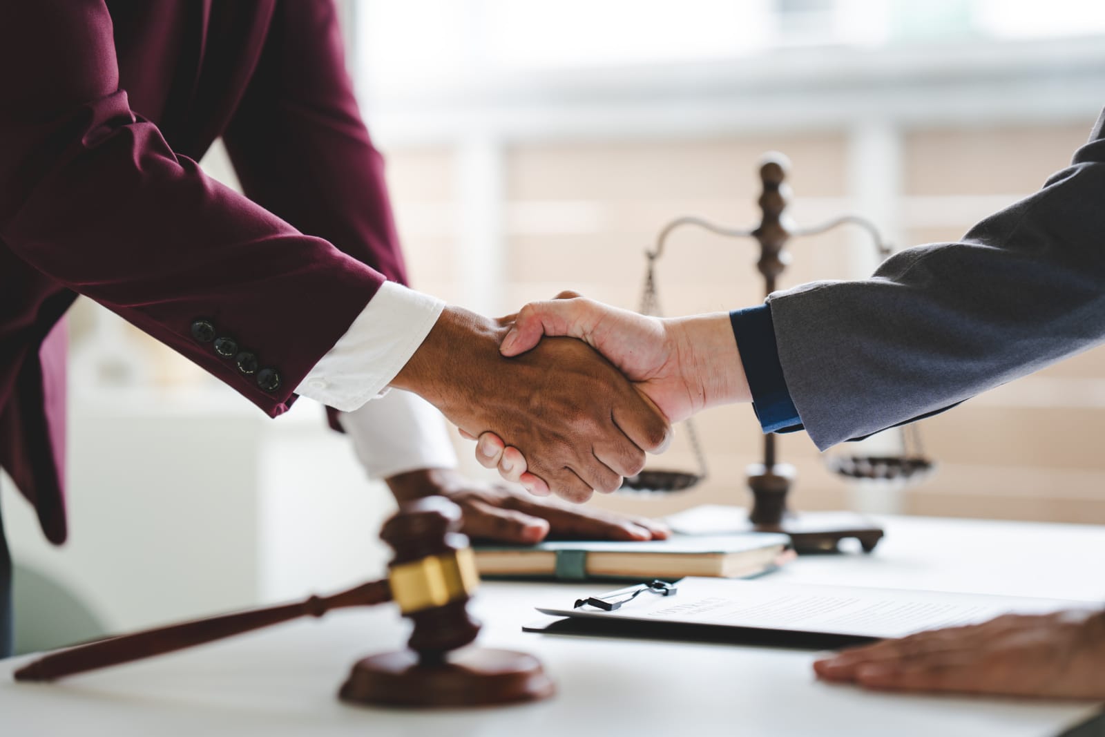 Close-up image of a lawyer and their client shaking hands across a desk after winning a motorcycle accident settlement.