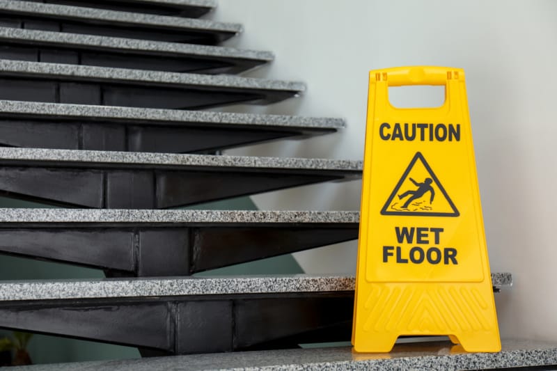 A sign that says "Caution: Wet Floor" at the bottom of a staircase inside a commercial building